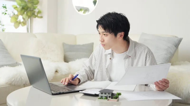 パソコンを見ながら紙を持つ男性